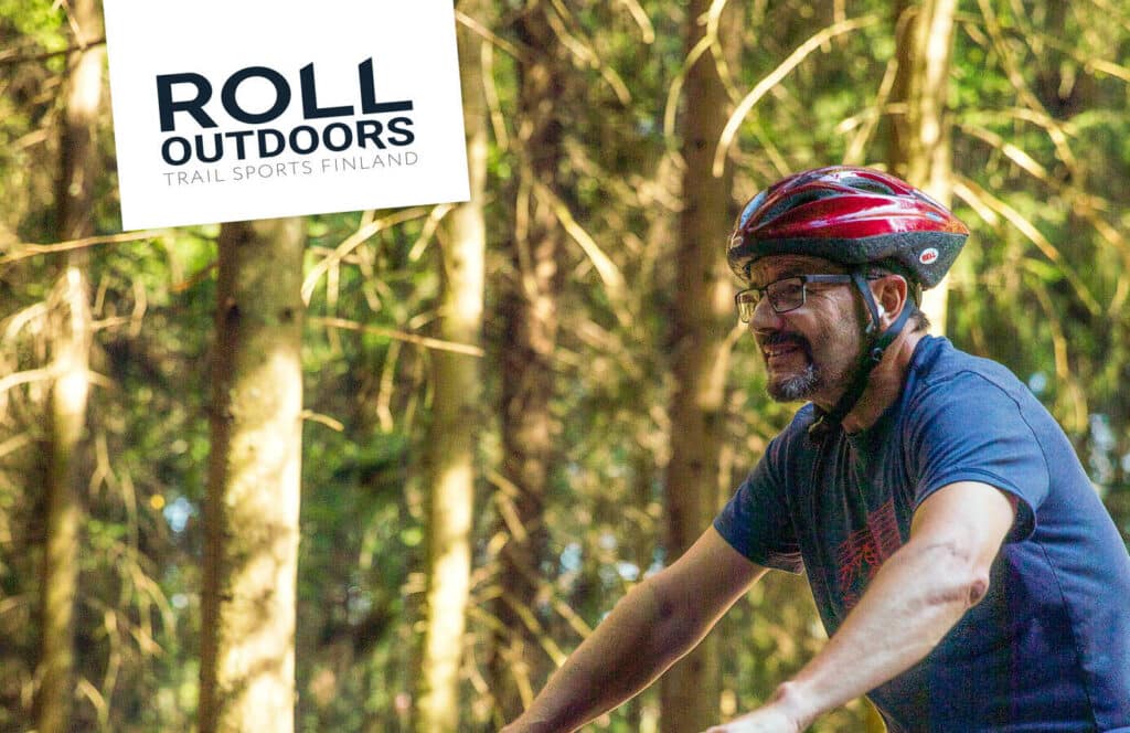Mies pyöräilee metsässä, taustalla Roll Outdoors -logo.